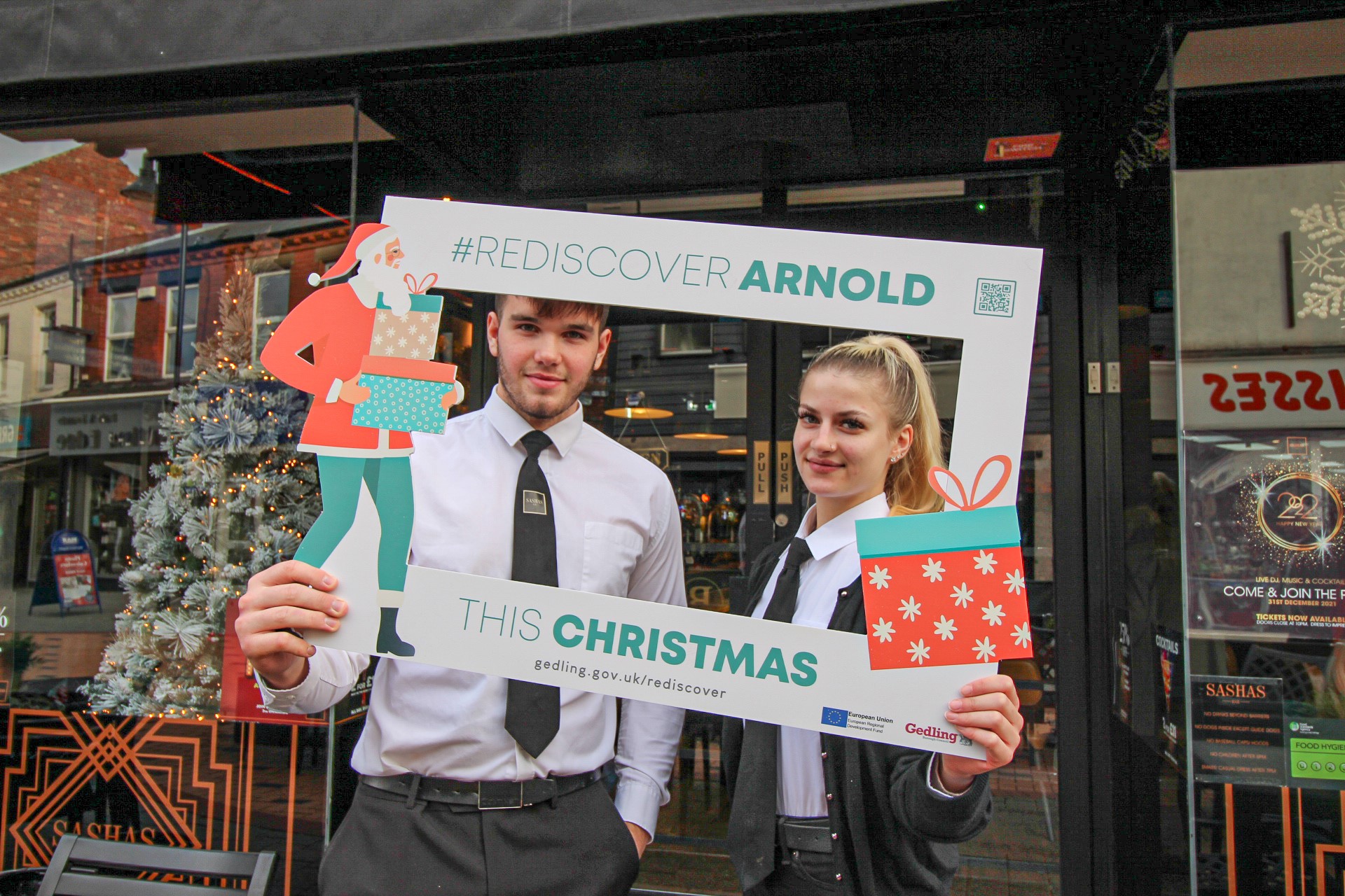 Two people stood outside bar holding a sign